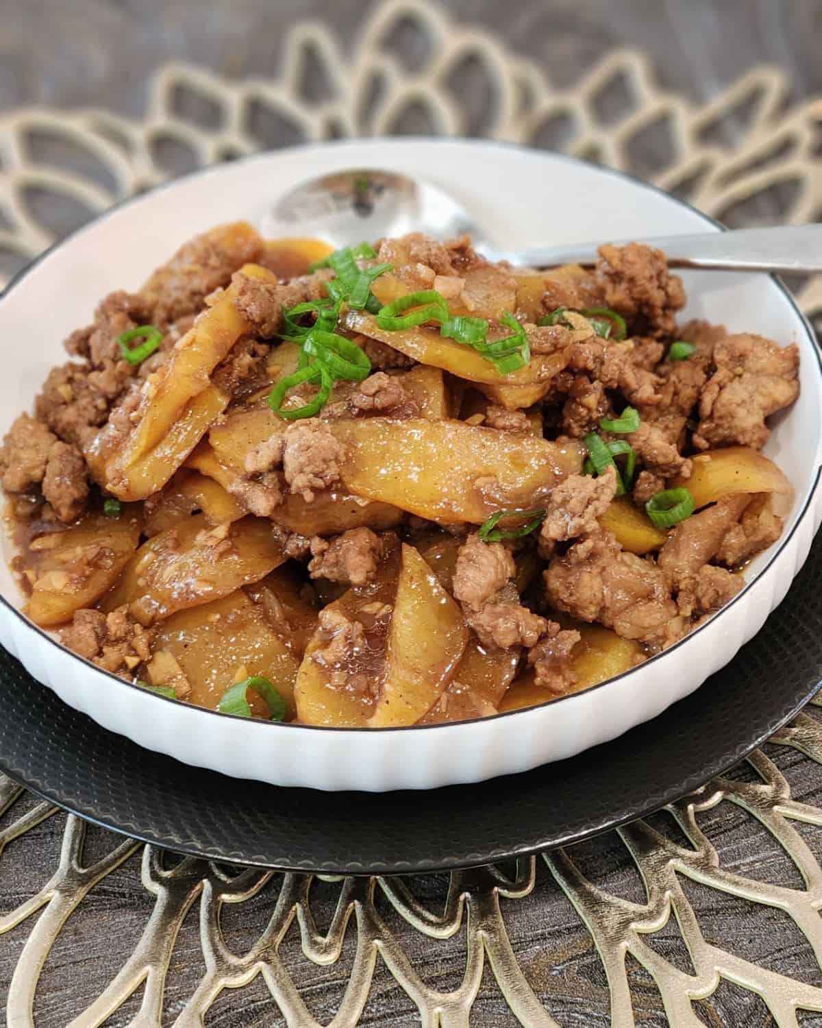 A plate of ground pork stir fry with potatoes with a spoon.