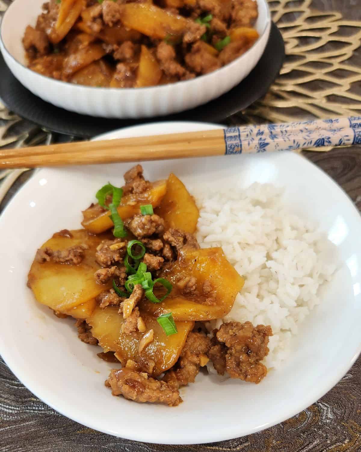 A small bowl of rice and ground pork stir fry with potatoes and chopsticks.