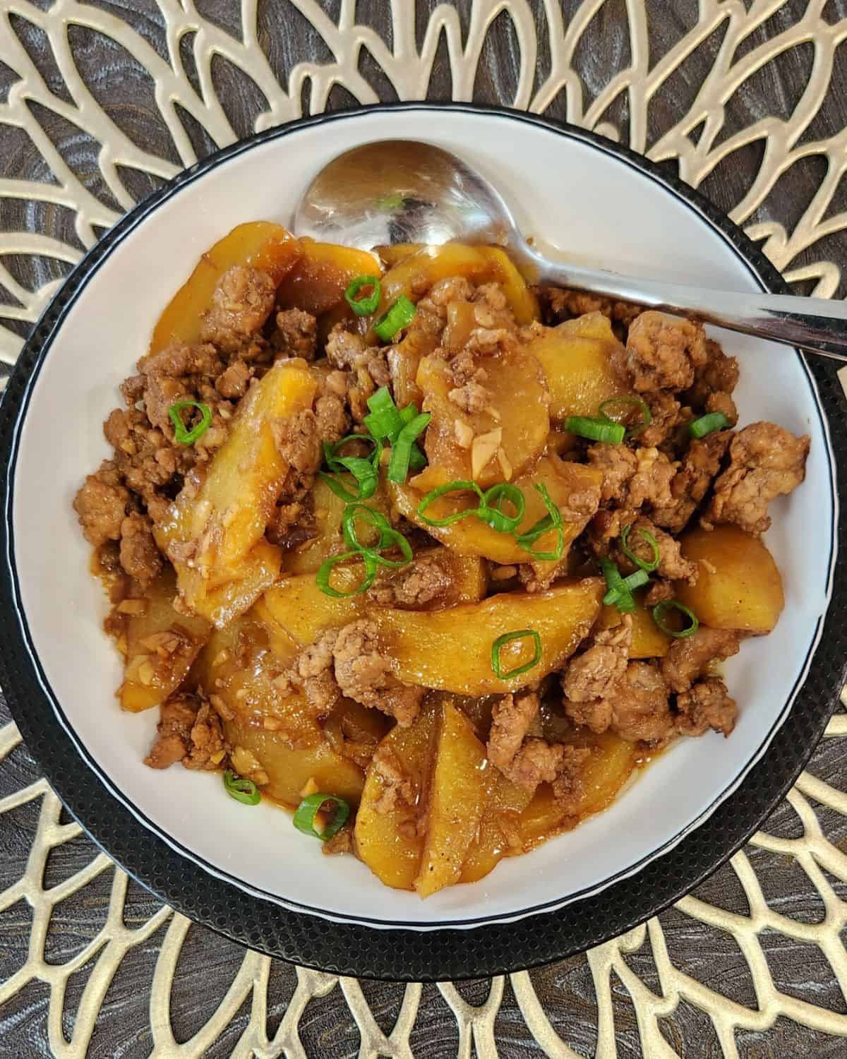 A plate of ground pork stir fry with potatoes and a spoon.