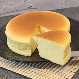 A slice of Japanese cheesecake after being cut in front of the whole loaf.