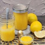 Two jars of lemon curd with lemon at the background.