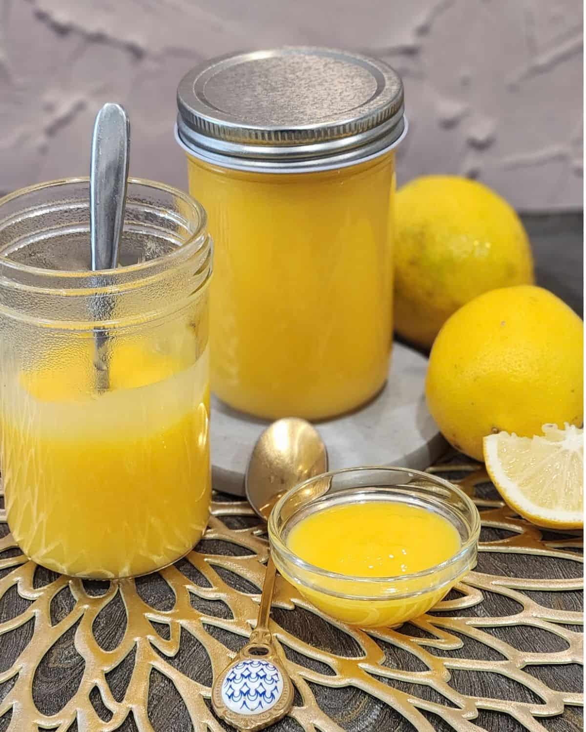 Two jars of lemon curd with lemon and small bowl of lemon curd.