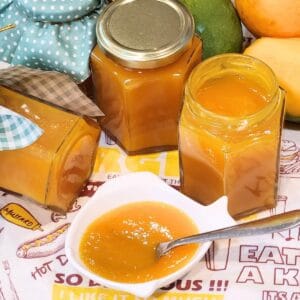 A few bottles of mango jam with some on a small plate.