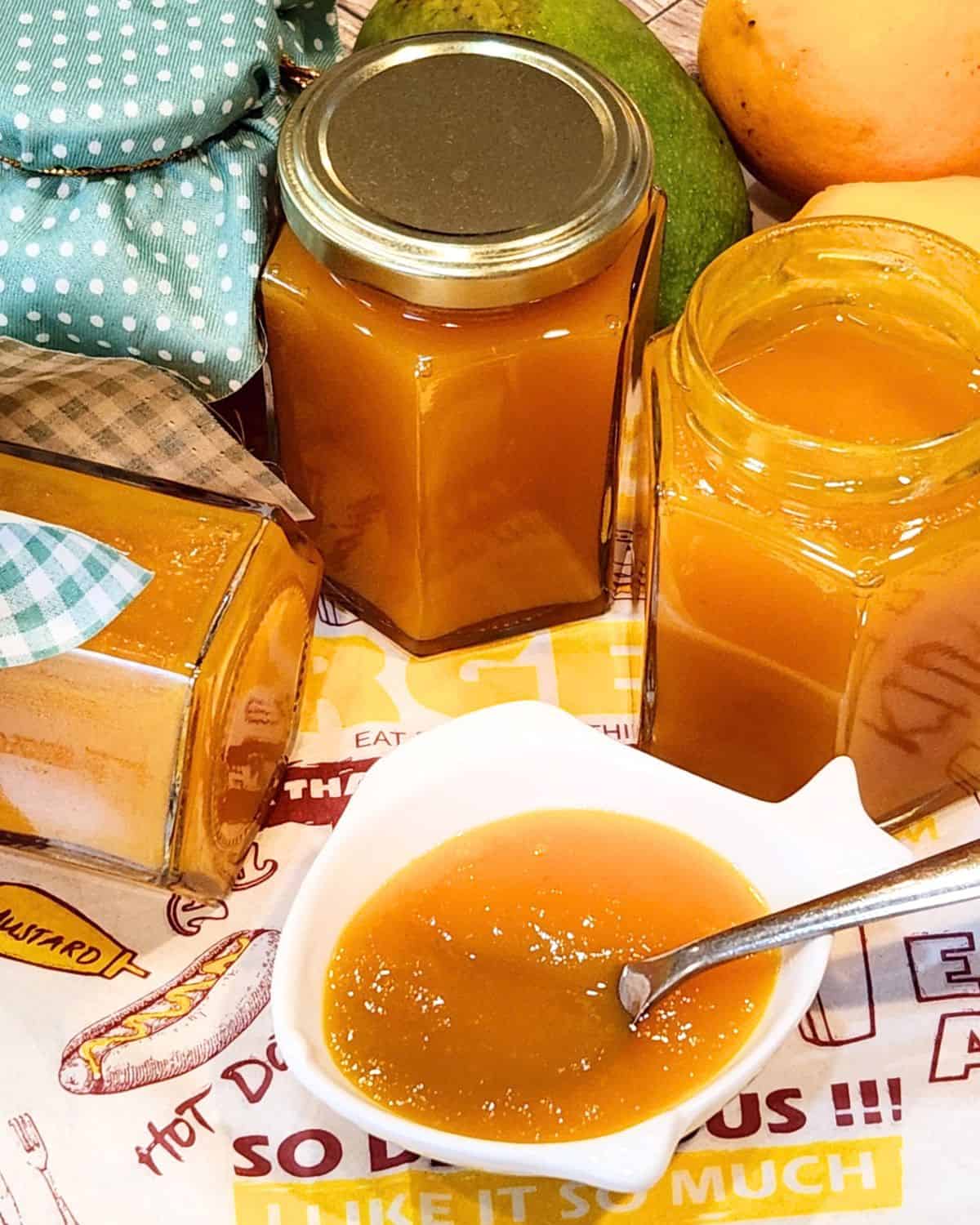 A few bottles of mango jam with some on a small plate.