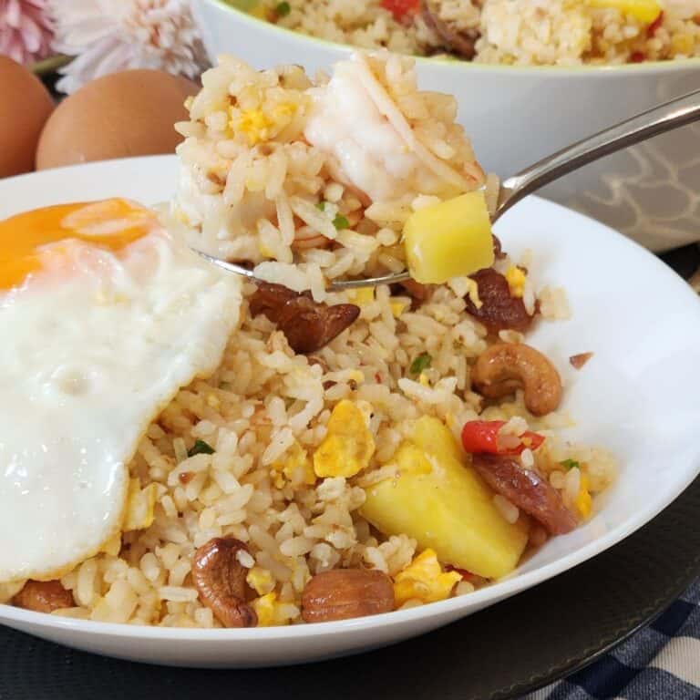 A plate of pineapple shrimp fried rice with fried egg on top.