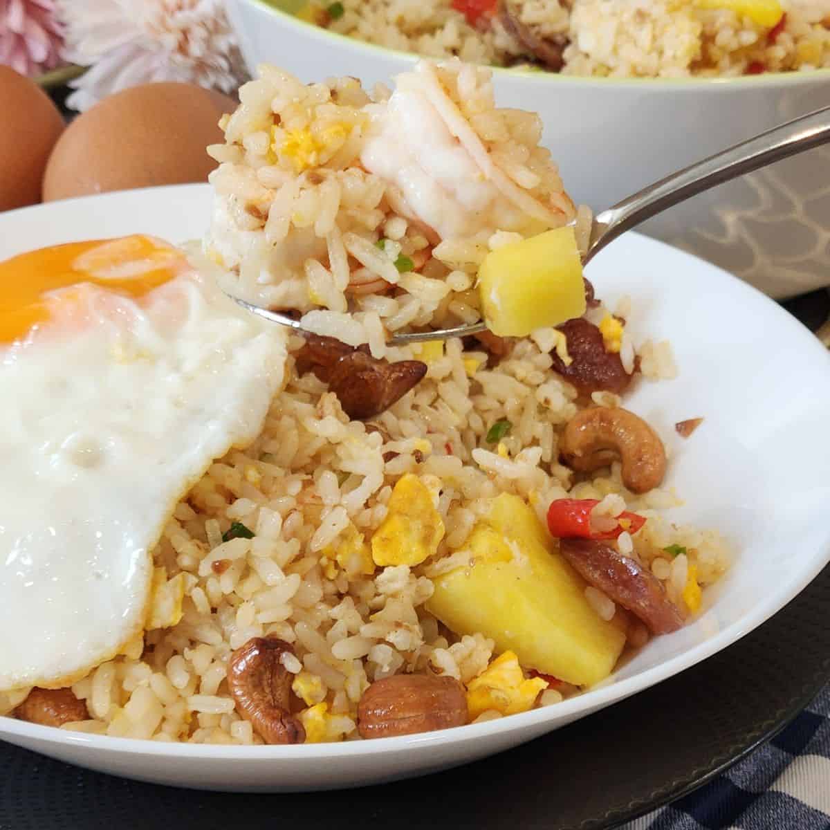 A plate of pineapple shrimp fried rice with fried egg on top.