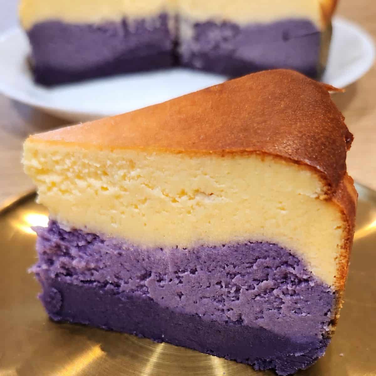 A slice of three-layered ube cheesecake on a golden plate.
