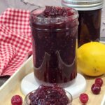 A jar full of cranbery jam with a small bow of cranberry jam.