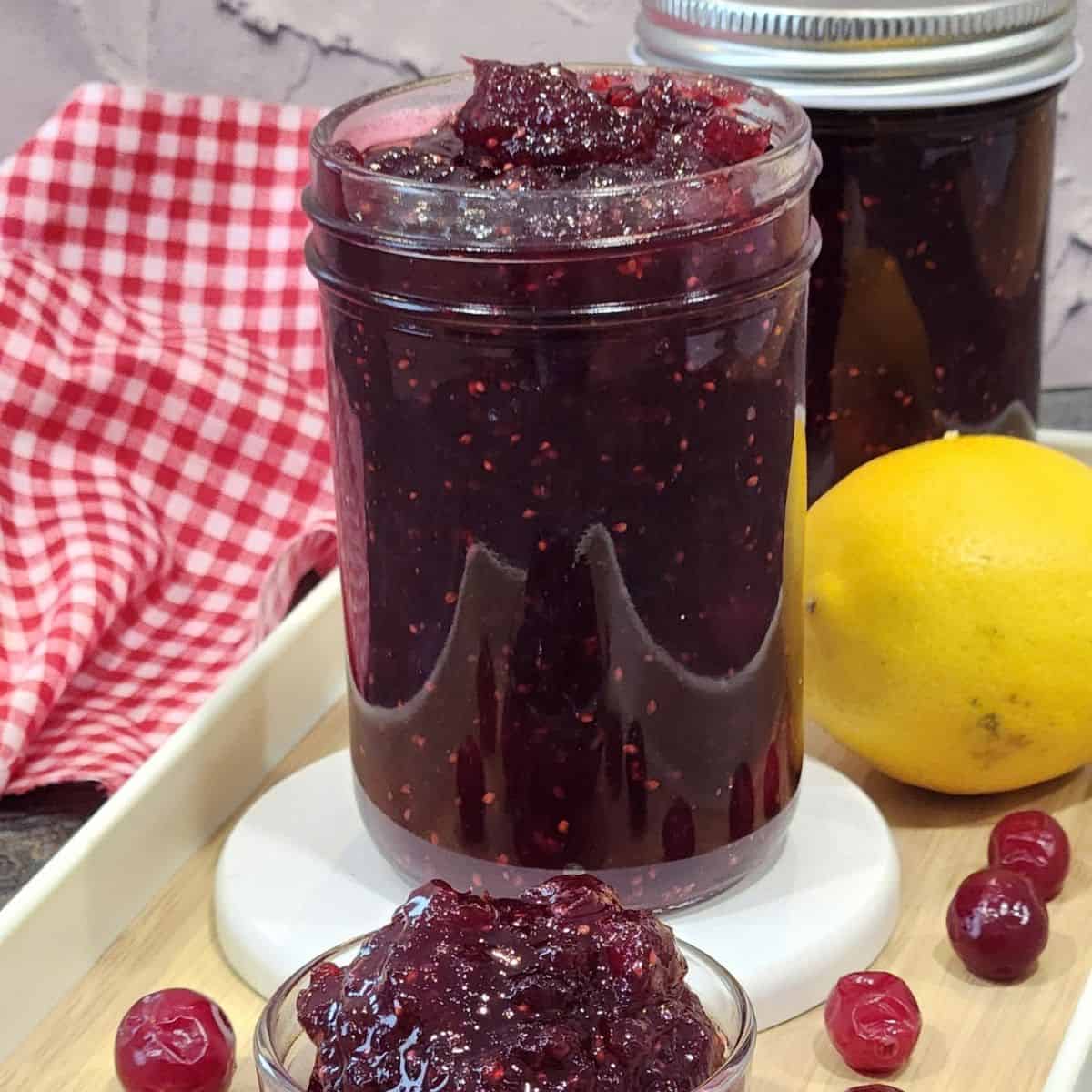 A jar full of cranbery jam with a small bow of cranberry jam.