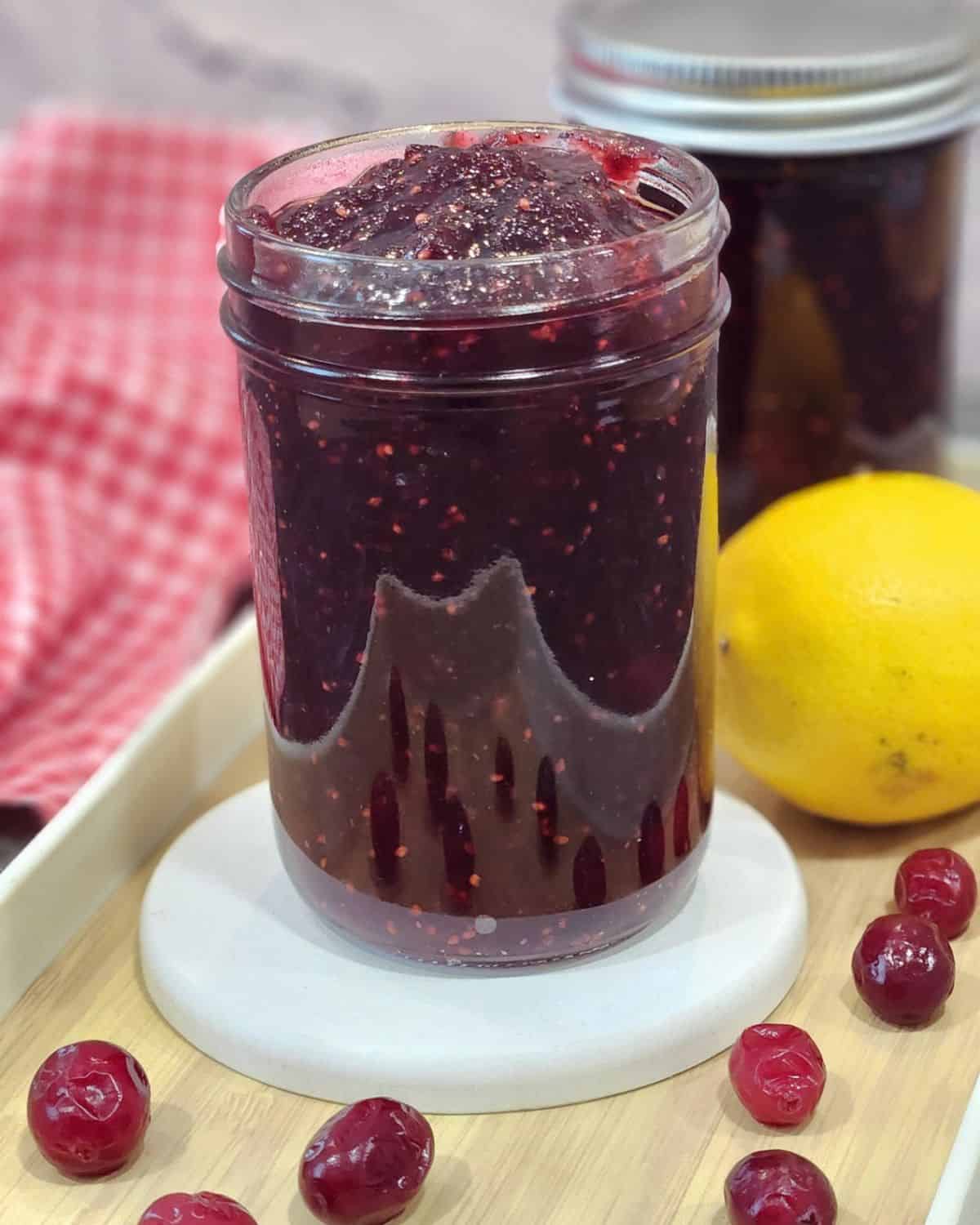 A jar full of cranberry jam with lemon at the back.