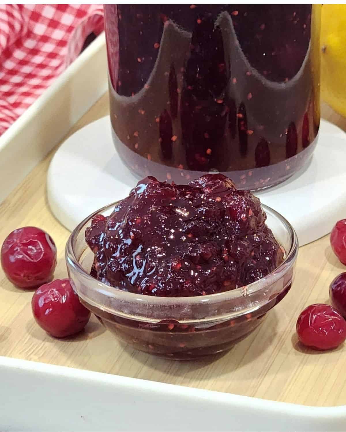 A small bowl of cranberry jam with frozen cranberries around.