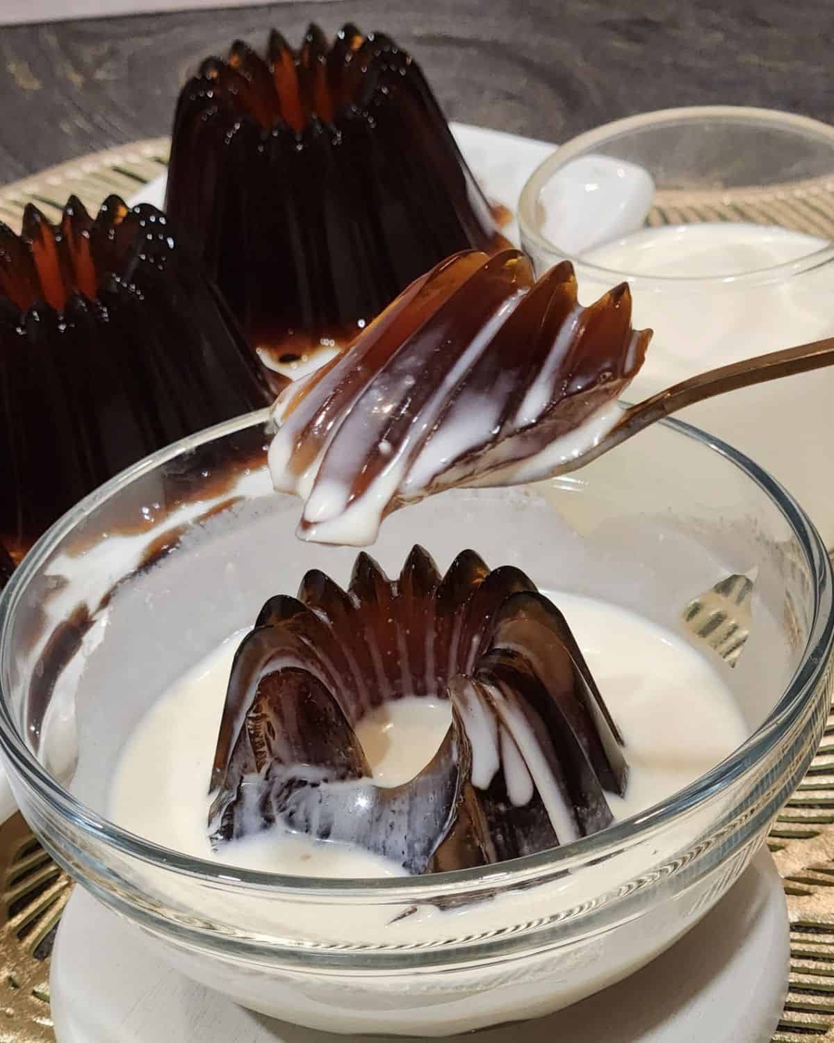 A golden spoon scooping Japanese coffee jelly with creamy milk sauce.