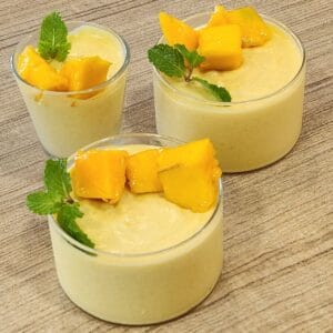 Three glasses of mango mousse decorated with mango cuts and mint leaves.
