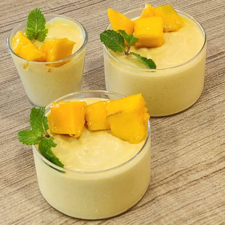 Three glasses of mango mousse decorated with mango cuts and mint leaves.