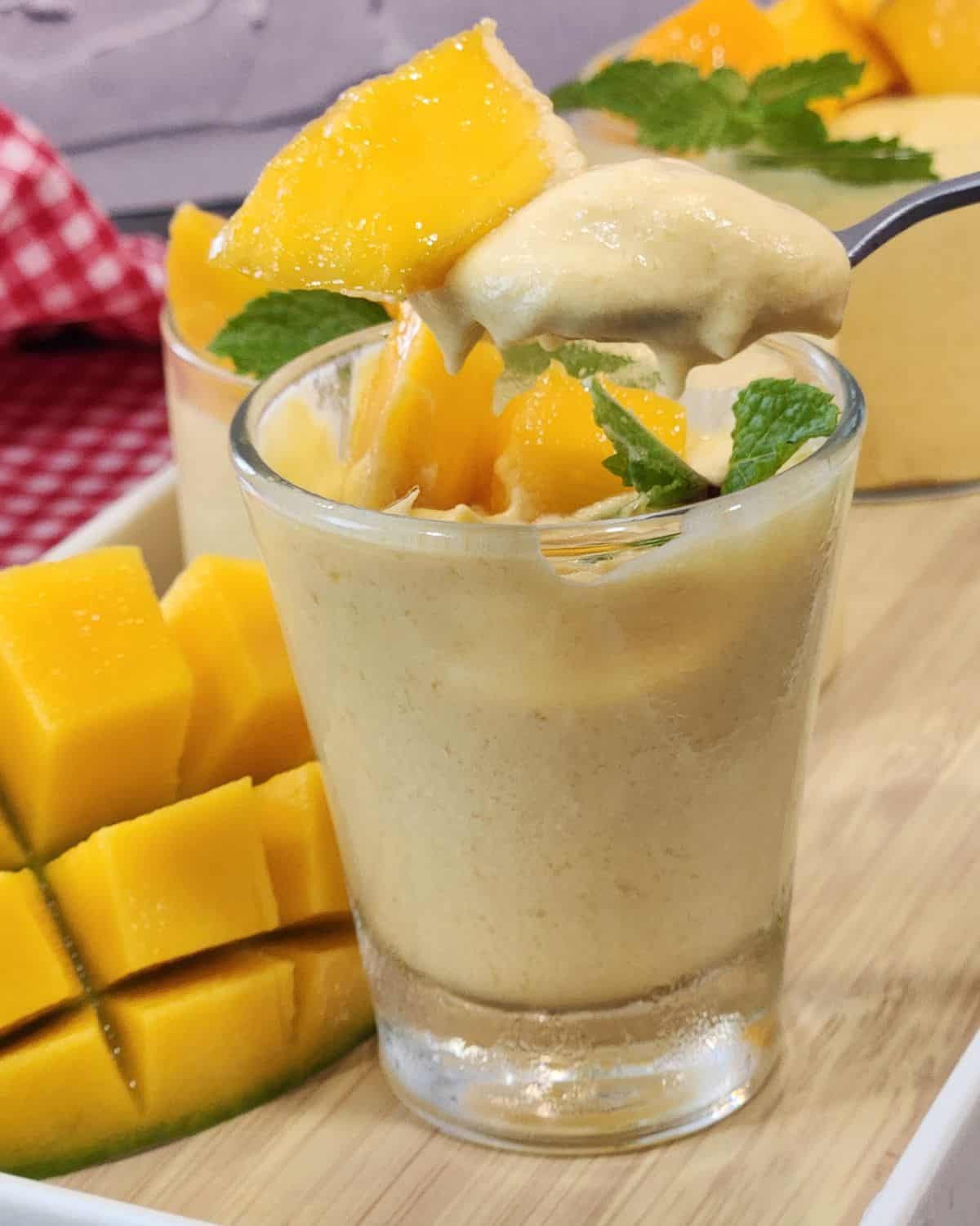 A spoon scooping mango mousse on top of a glass.