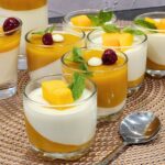 Mini glasses of mango panna cotta decorated with mango and mint leaves.