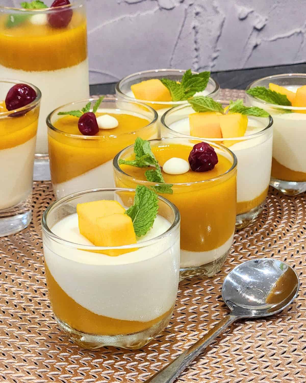 Mini glasses of mango panna cotta decorated with mango cubes and mint leaves.