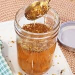 A golden spoon with drizzling osmanthus syrup on top of a jar.