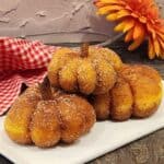 A stack of three pumpkin donuts with the shape of pumpkin and cinnamon stick as stems.