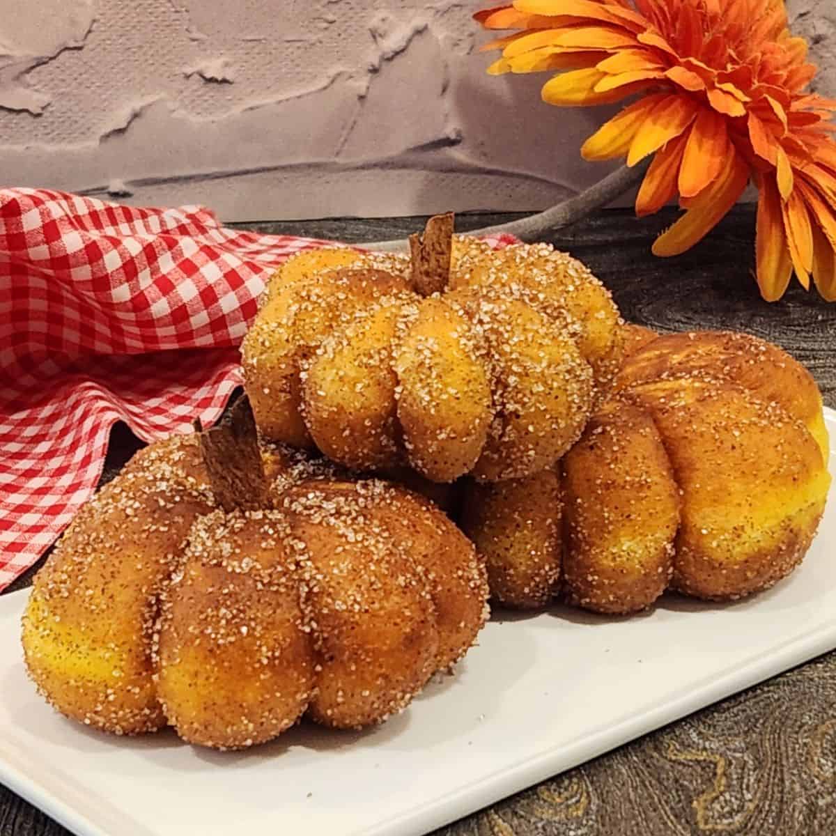 A stack of three pumpkin donuts with the shape of pumpkin and cinnamon stick as stems.