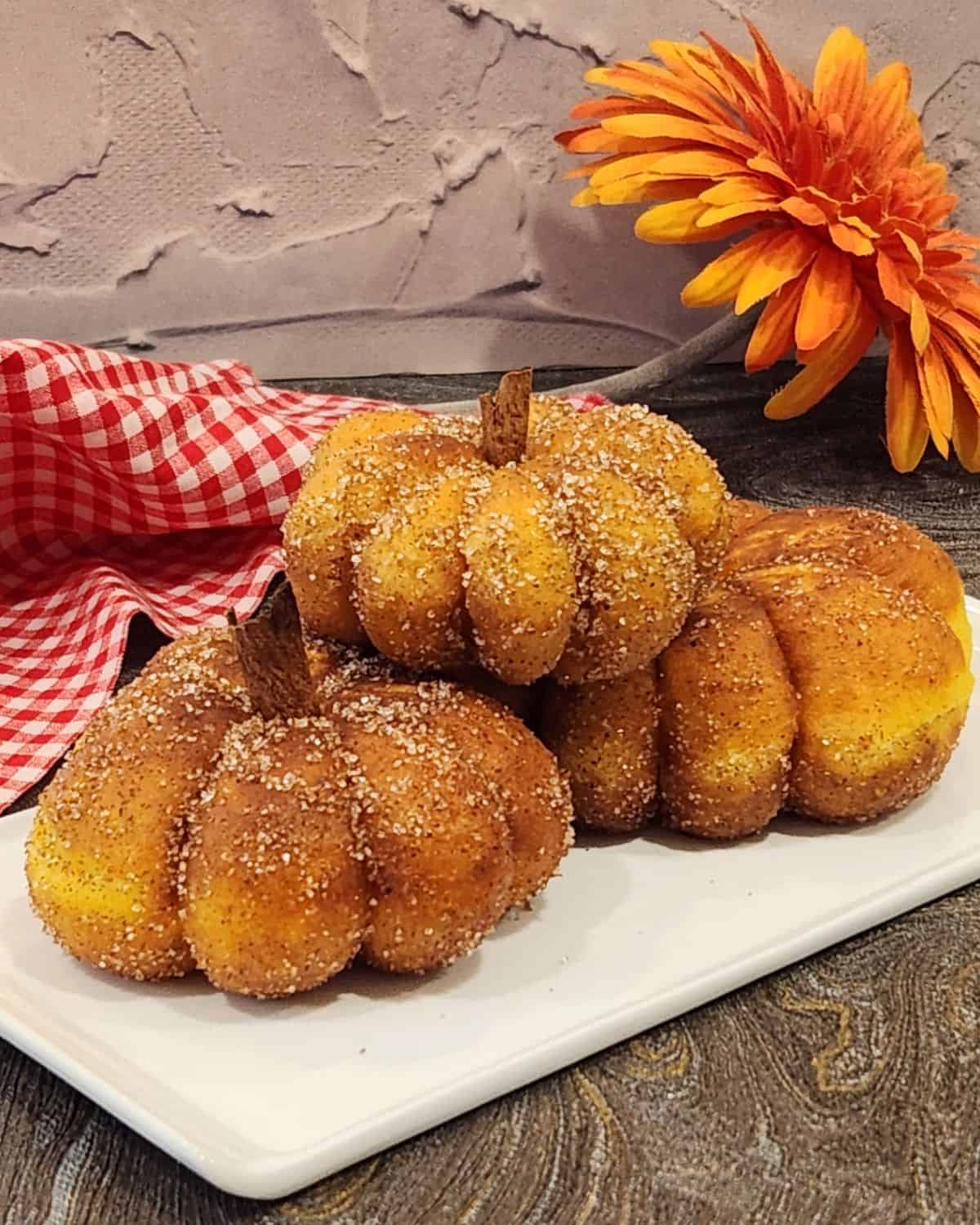 A stack of three pumpkin donuts with the shape of pumpkin and cinnamon stick as stems.
