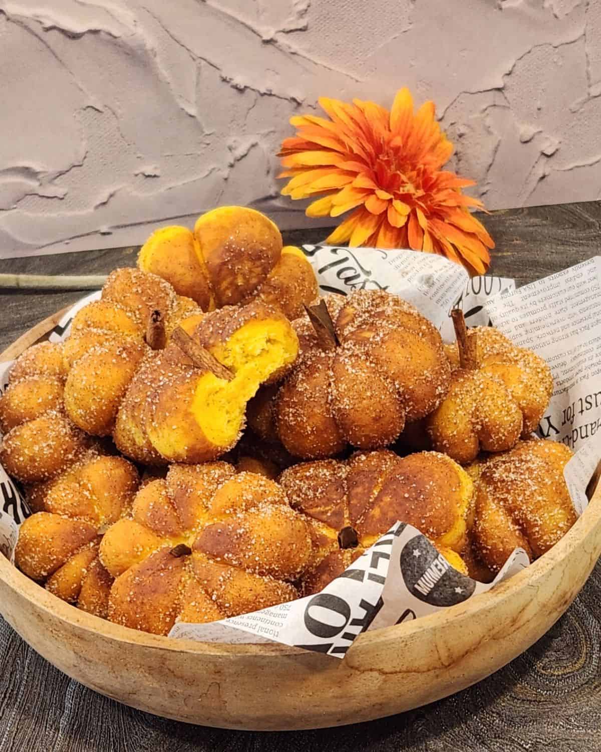 A stack of pumpkin donuts in a wooden basket, with one half eaten on top.