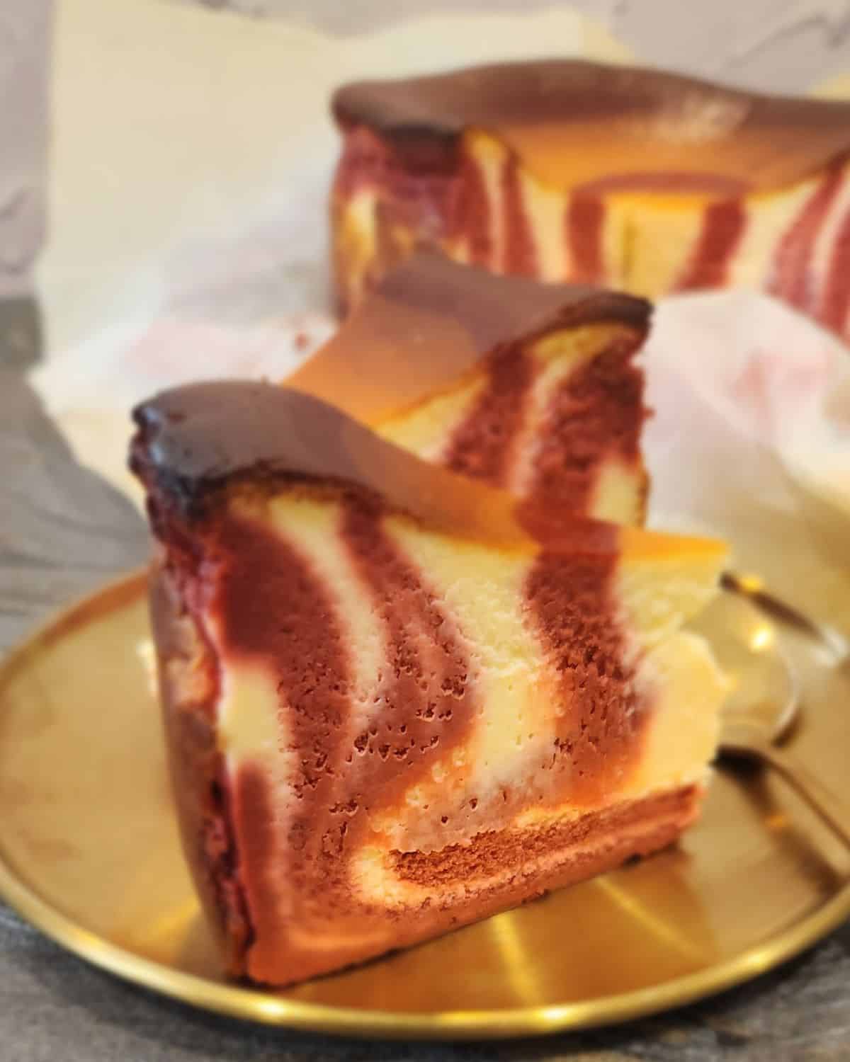A close up look of a slice of red velvet cheesecake on a golden plate.